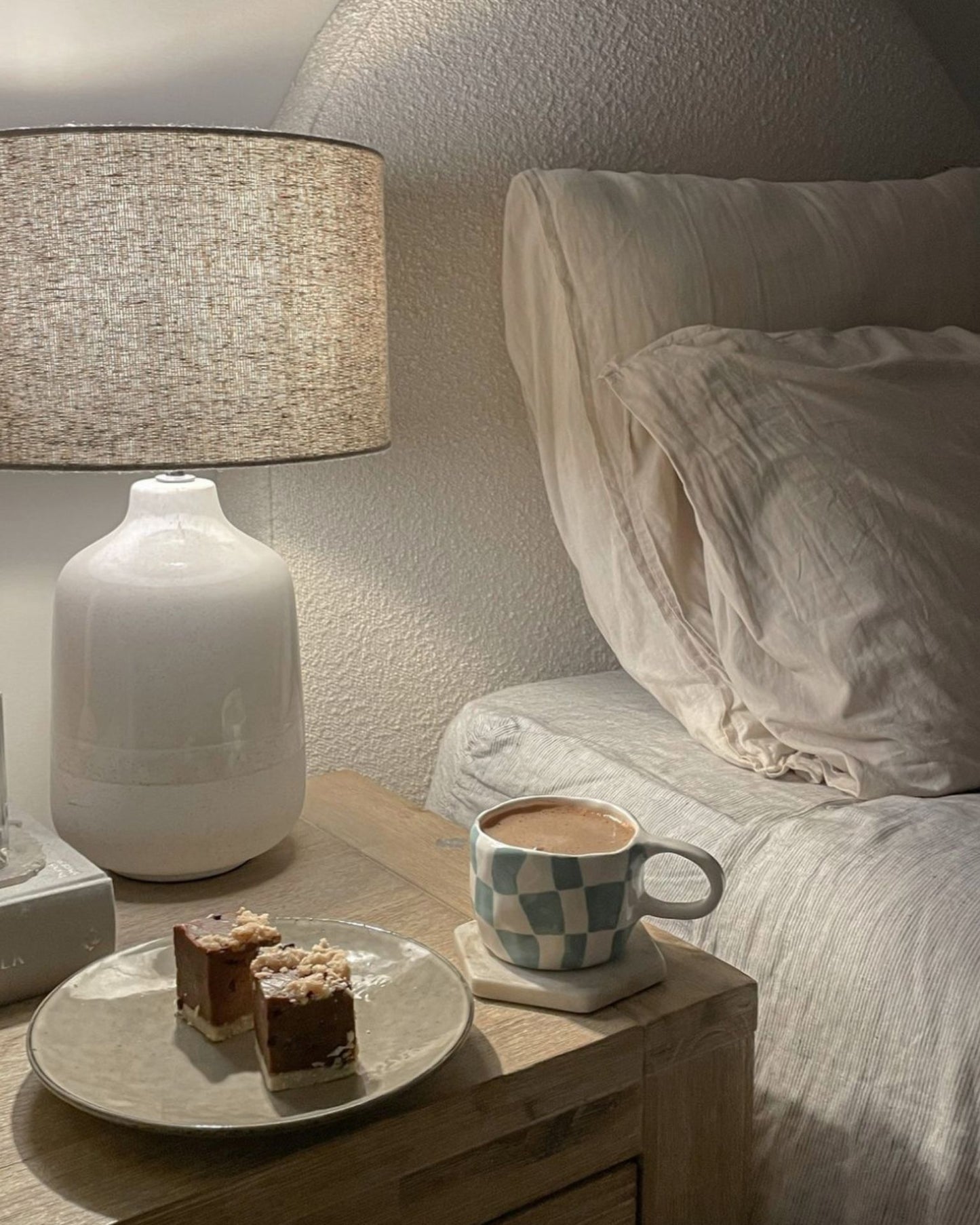 Cosy bedside scene featuring a mug of Real Rad Food Rad Sleep sleepy hot chocolate beside raw slices and a warm bedside lamp for a relaxing nighttime ritual