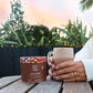 Hands holding a mug of Real Rad Food Rad Sleep sleepy hot chocolate beside a Rad Sleep botanical supplement tub during a calming sunset nighttime ritual