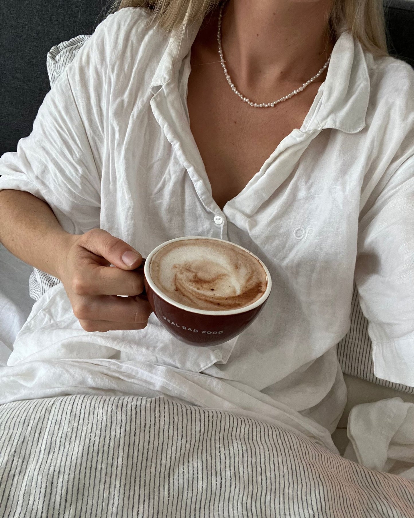 Women in bed holding a mug of Real Rad Food Rad Sleep sleepy hot chocolate in bed as part of a calming nighttime wellness routine